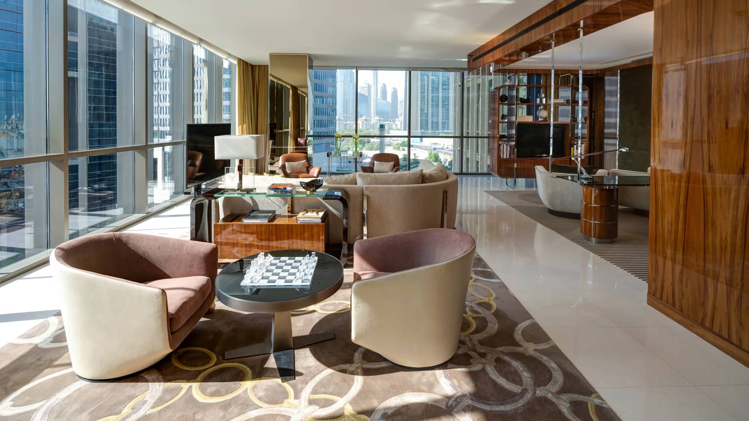 Large, long living room with cream arm chairs and sofa, corner wall of windows