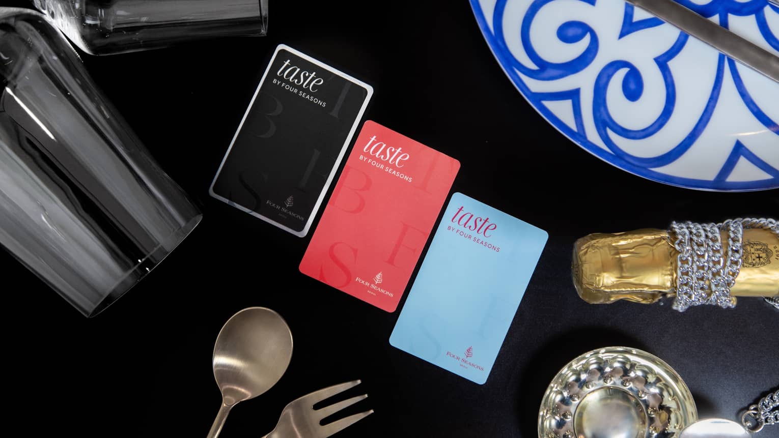 Three colours of Taste by Four Seasons cards on table with black tablecloth, stemmed wine glasses and silver cutlery