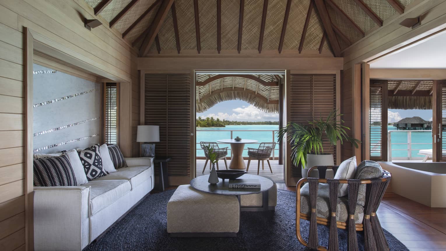Living room with thatched roof, white sofa, arm chair, coffee table, view of turquoise lagoon