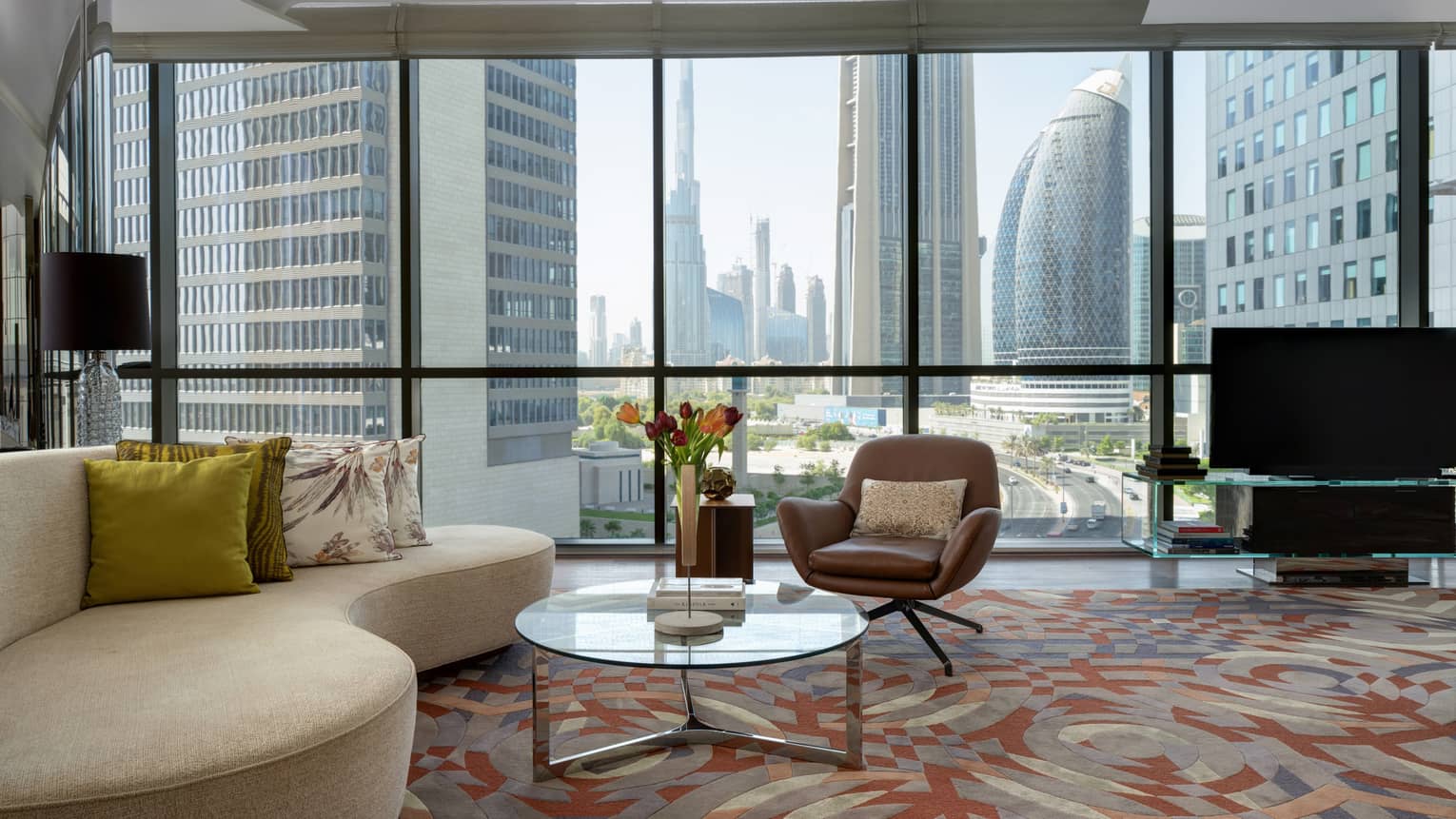 Living area with curved sofa, arm chair, glass table, wall of windows