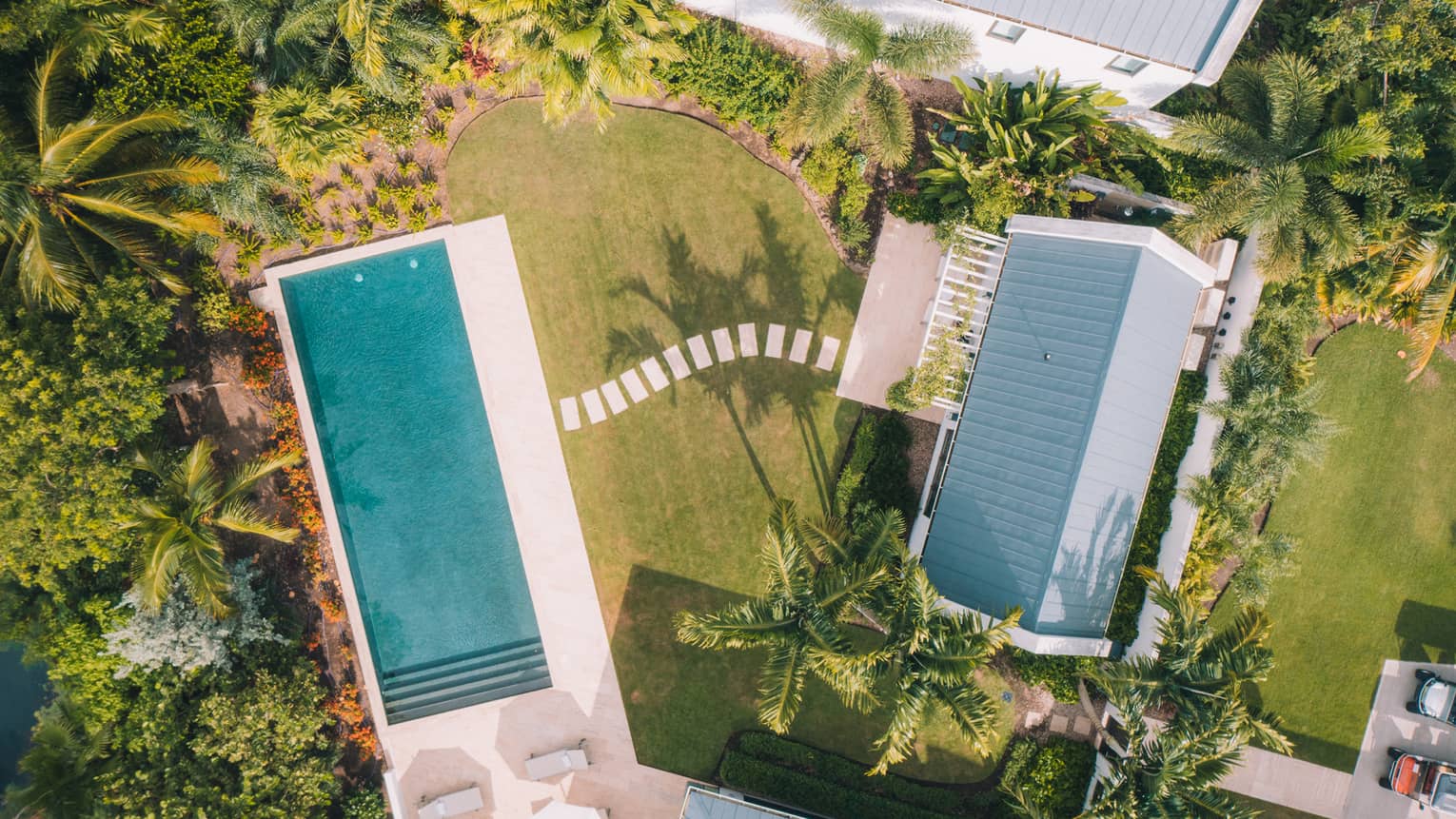 Aerial view of home and rectangular pool, surrounded by green palm trees