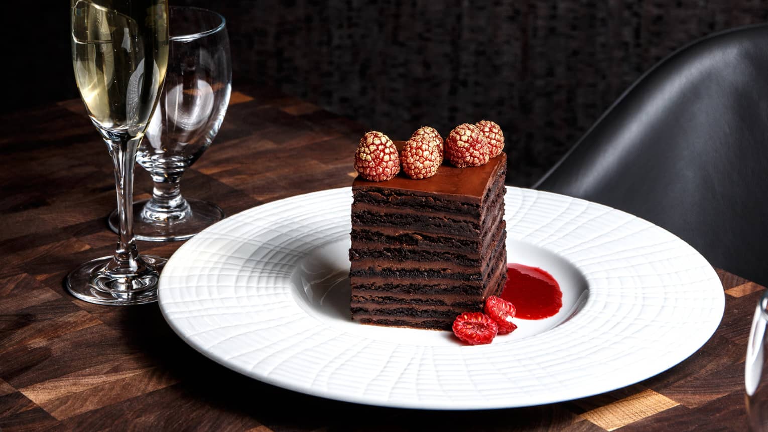 Layered chocolate desert on a white plate next to a flute of champagne and glass of water