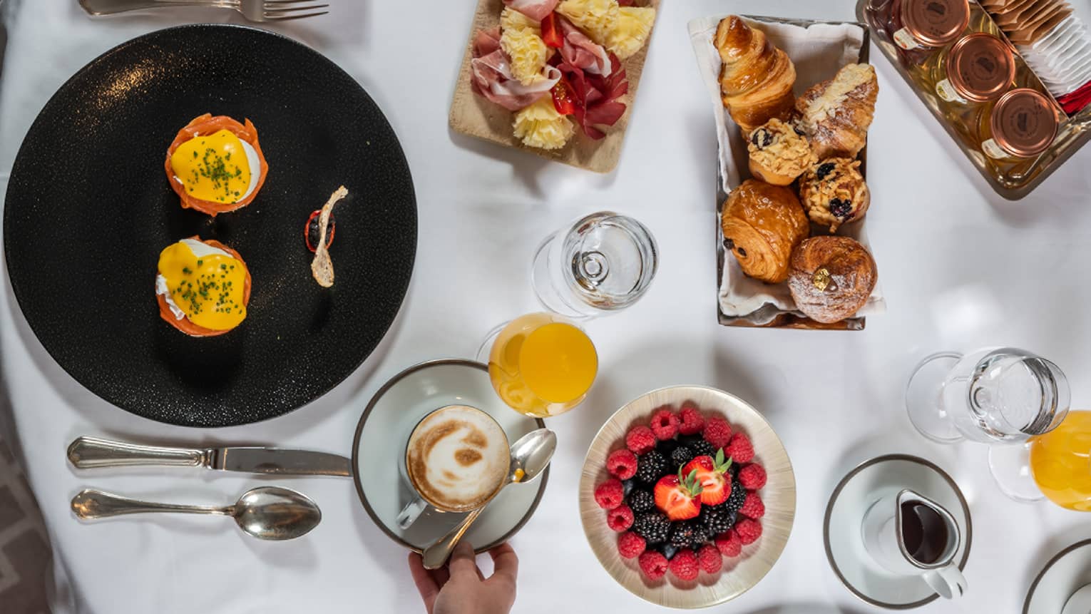 Aerial view of brunch dishes, fruit, juices, water set on white tablecloth
