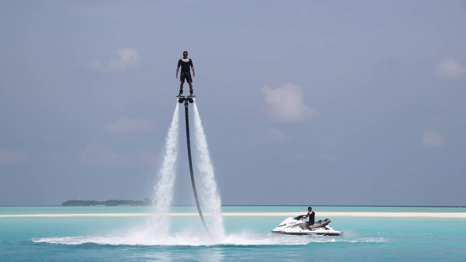 Person hovers suspended in air above ocean on X Jetblade pack, near jetski