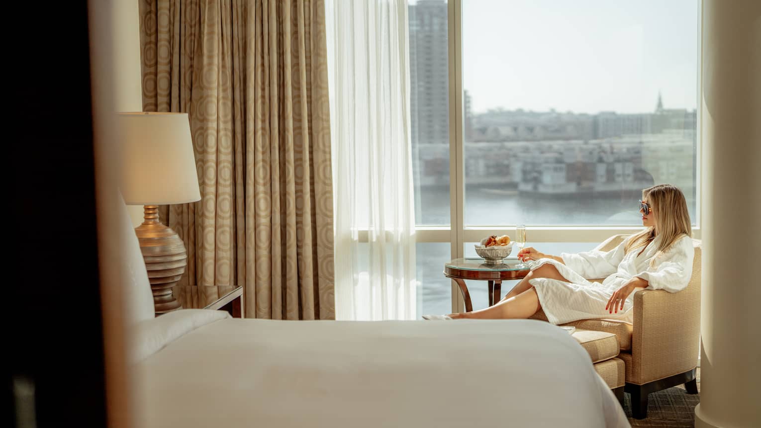 A guest sitting in a chair near a floor-to-ceiling window and holding a glass of wine