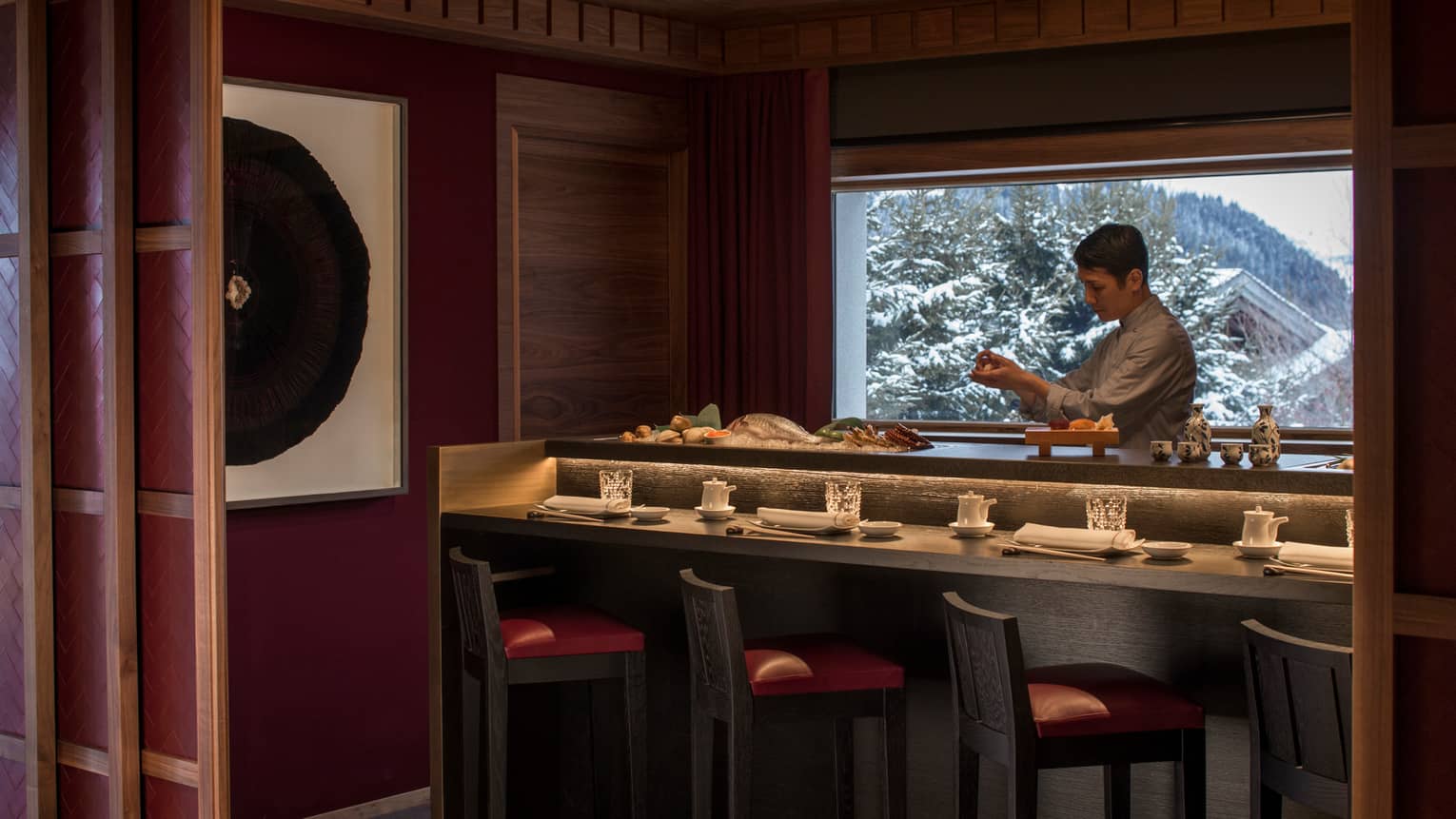 Kaito sushi chef at small bar with fresh whole fish, seafood, window with winter mountain views