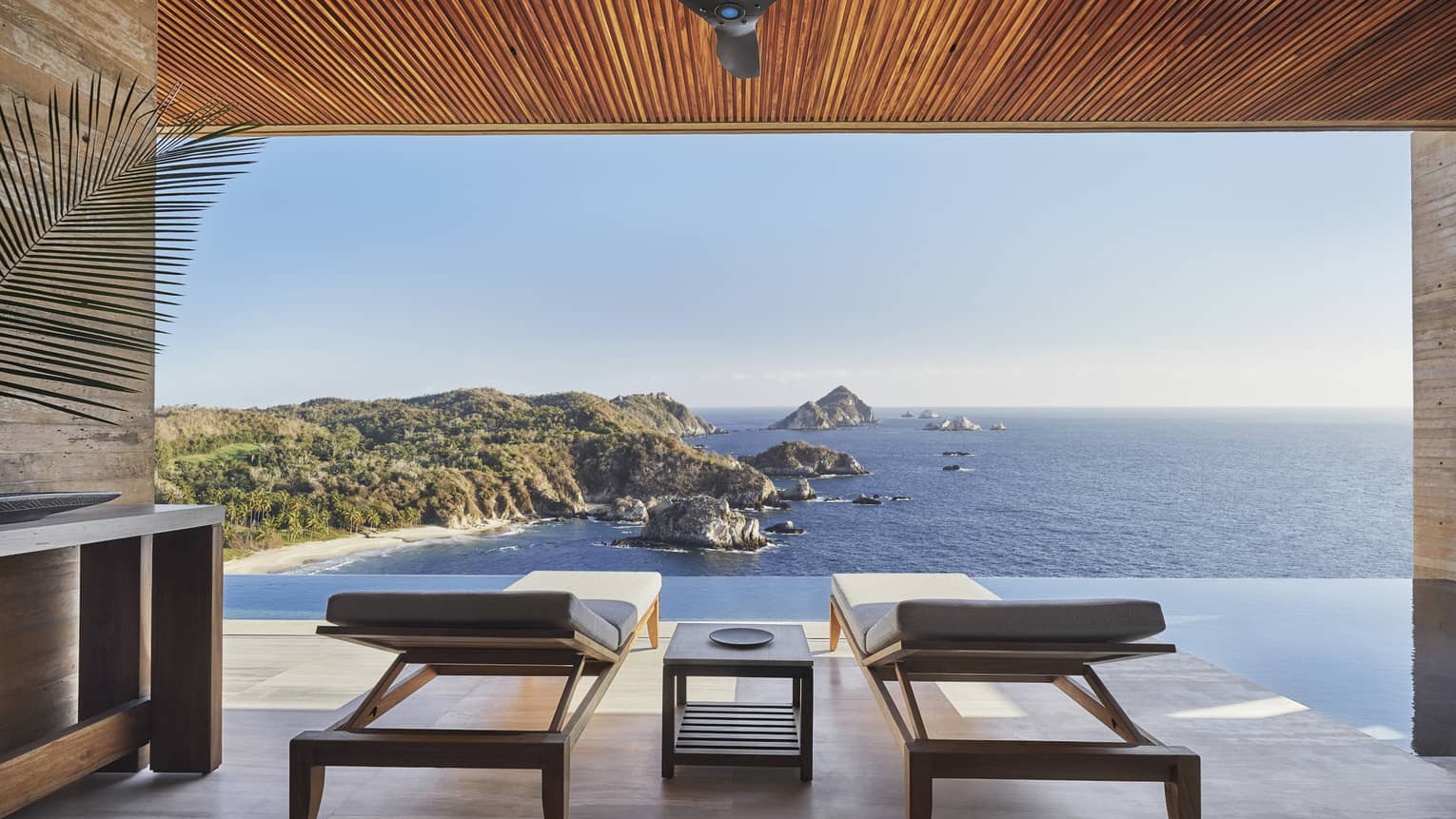 Two lounge chairs under a covered terrace at elevated position face outwards to ocean view in Tamarindo, Mexico