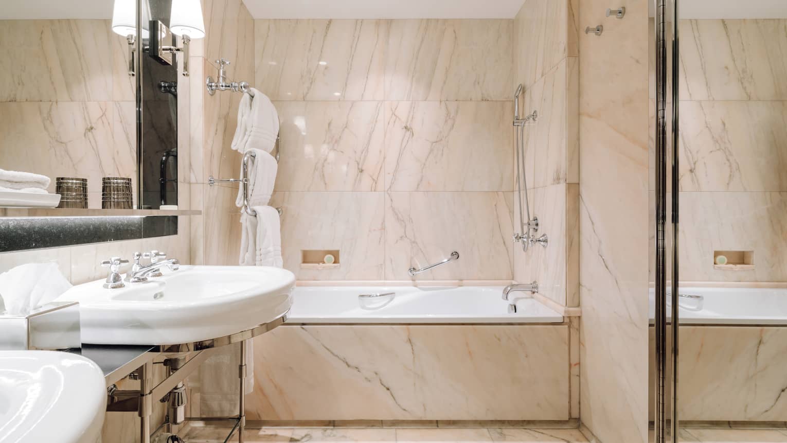 Bathroom with marble walls, a bathtub with shower, dual sinks and neatly arranged towels and bathrobes.