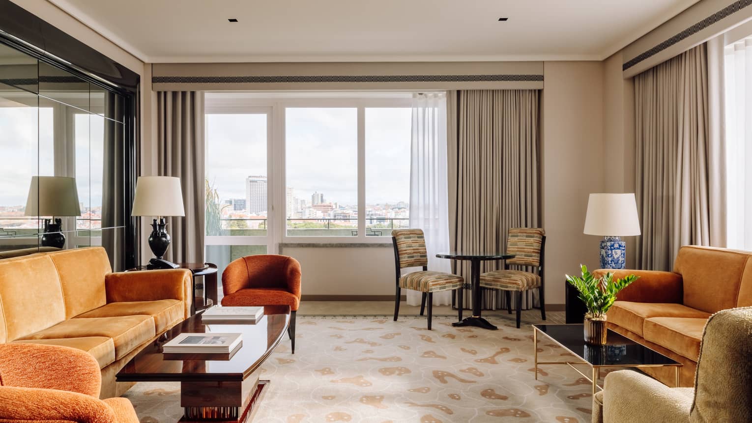 Spacious hotel suite living room with multiple sofas, armchairs, coffee tables and large windows with city views.