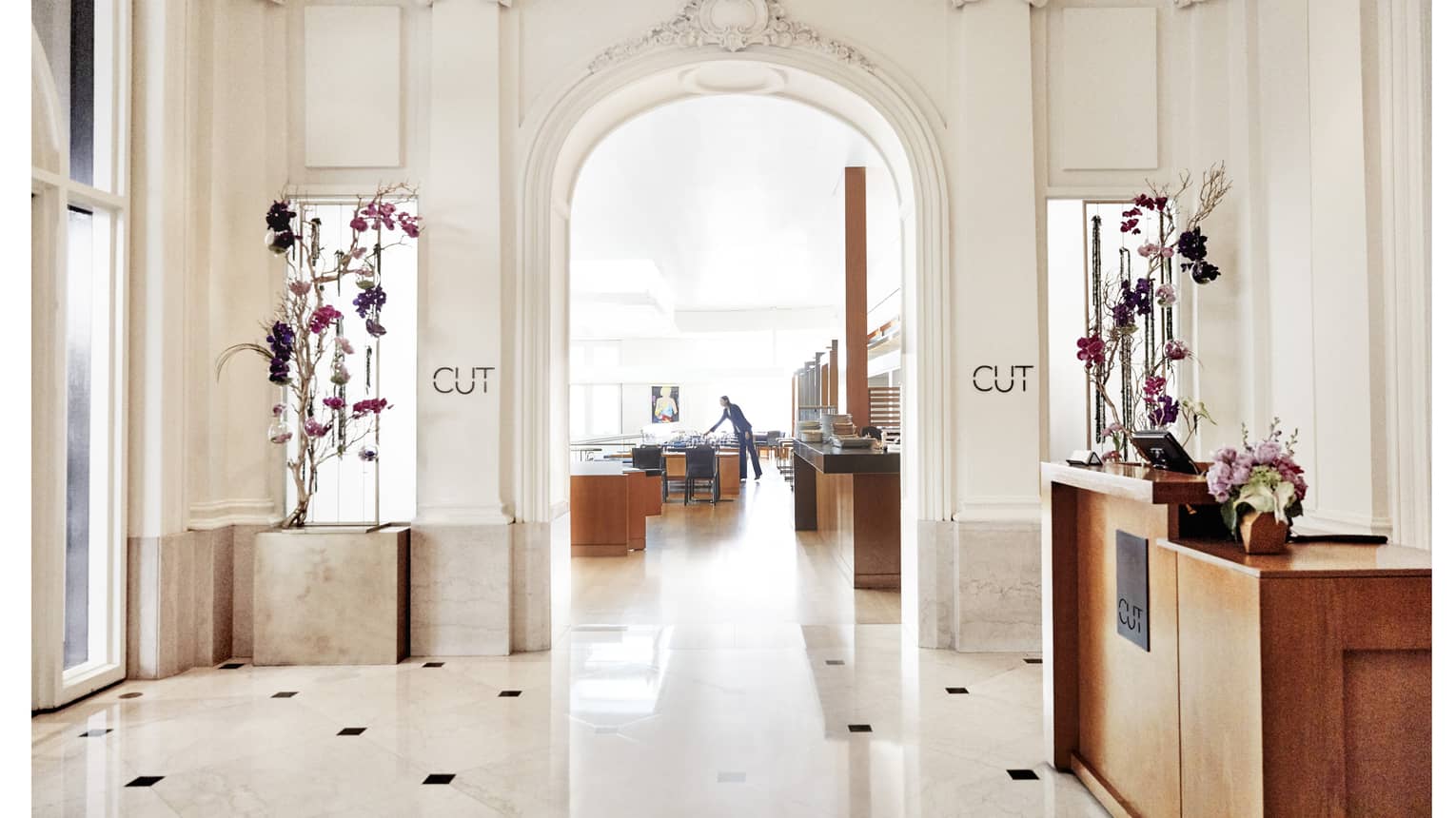 A brightly lit restaurant entrance with cream walls and floor, and a host station made of bright wood.