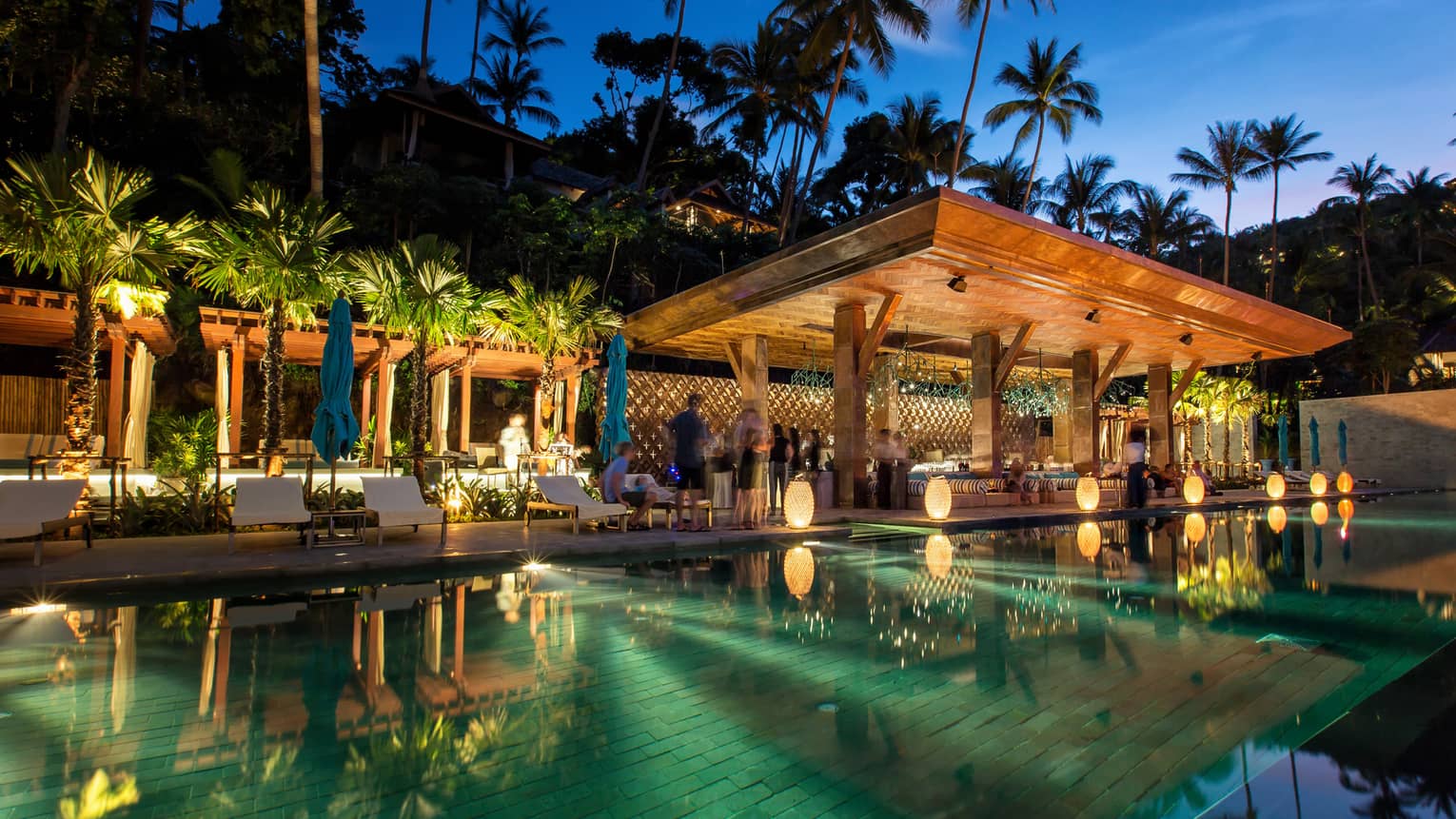 People mingle at CocoRum Bar at dusk, mirror-like pool in foreground 