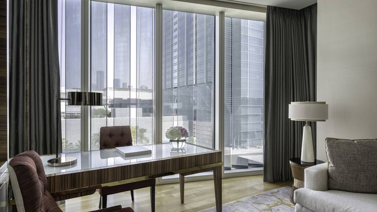 Desk and two upholstered chairs next to wall of windows in luxury hotel suite