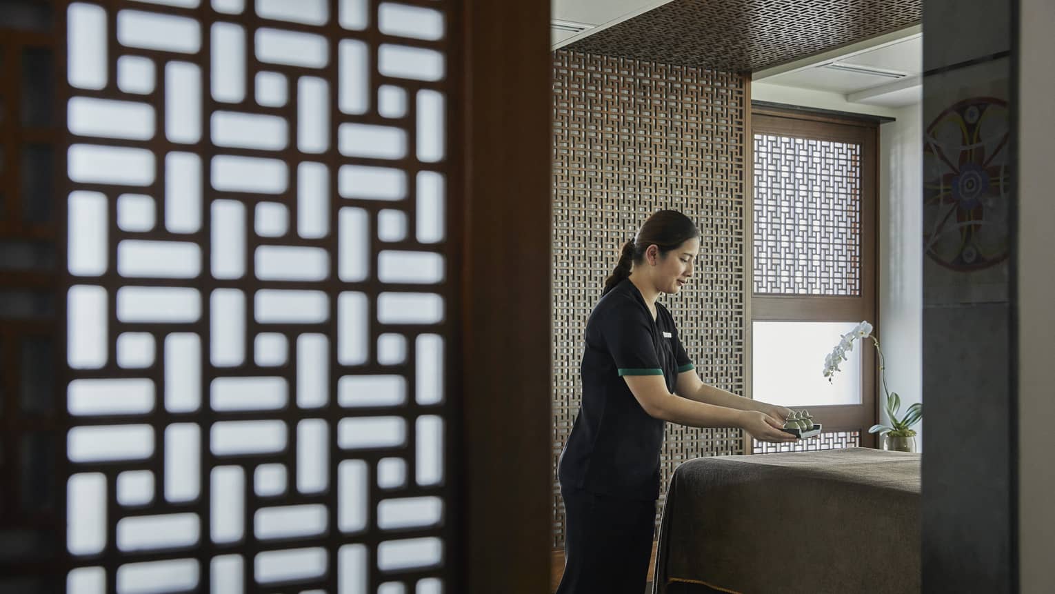A female esthetician prepares a bed in the massage room.