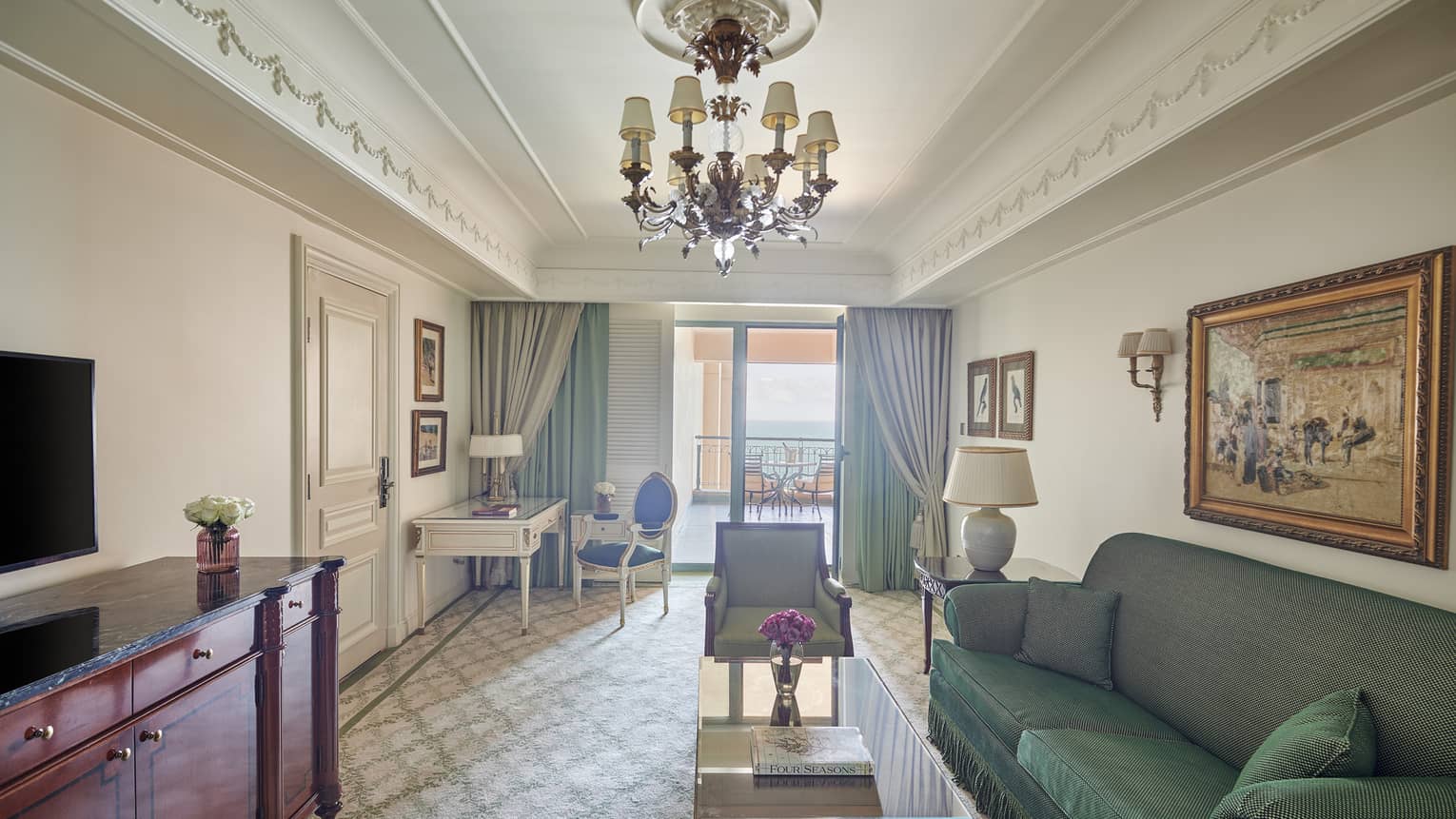Four Seasons Suite living area with green sofa, twin armchairs, corner desk and chair, glass door to veranda