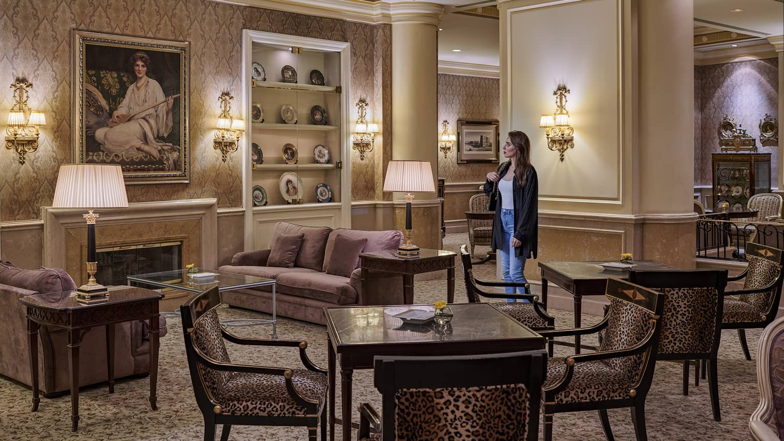 Woman stands in a lounge featuring two dark wood square tables, each with four chairs, two purple sofas