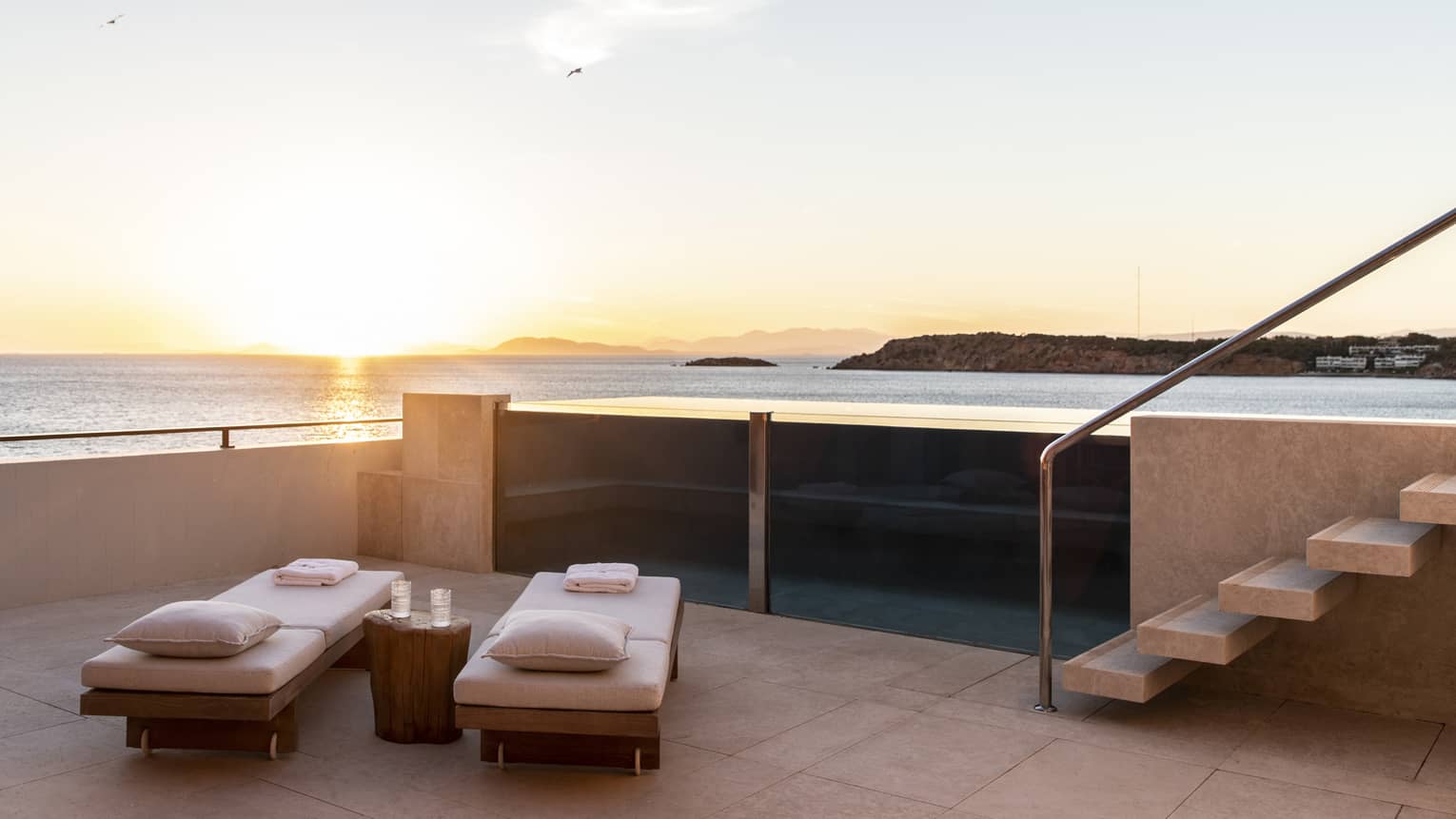 Raised, glass-enclosed pool on a private terrace at sunset overlooking the sea