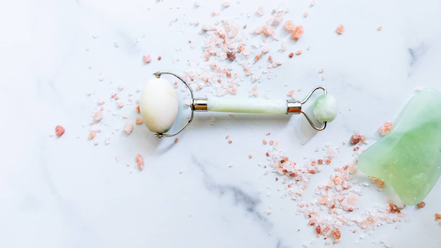 a spa roller tool on a white marble counter surrounded by himalayan salt