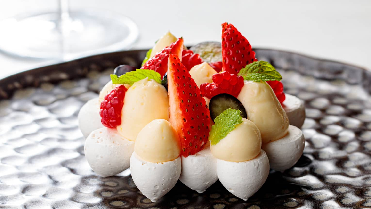 Custard with strawberries on a black plate.