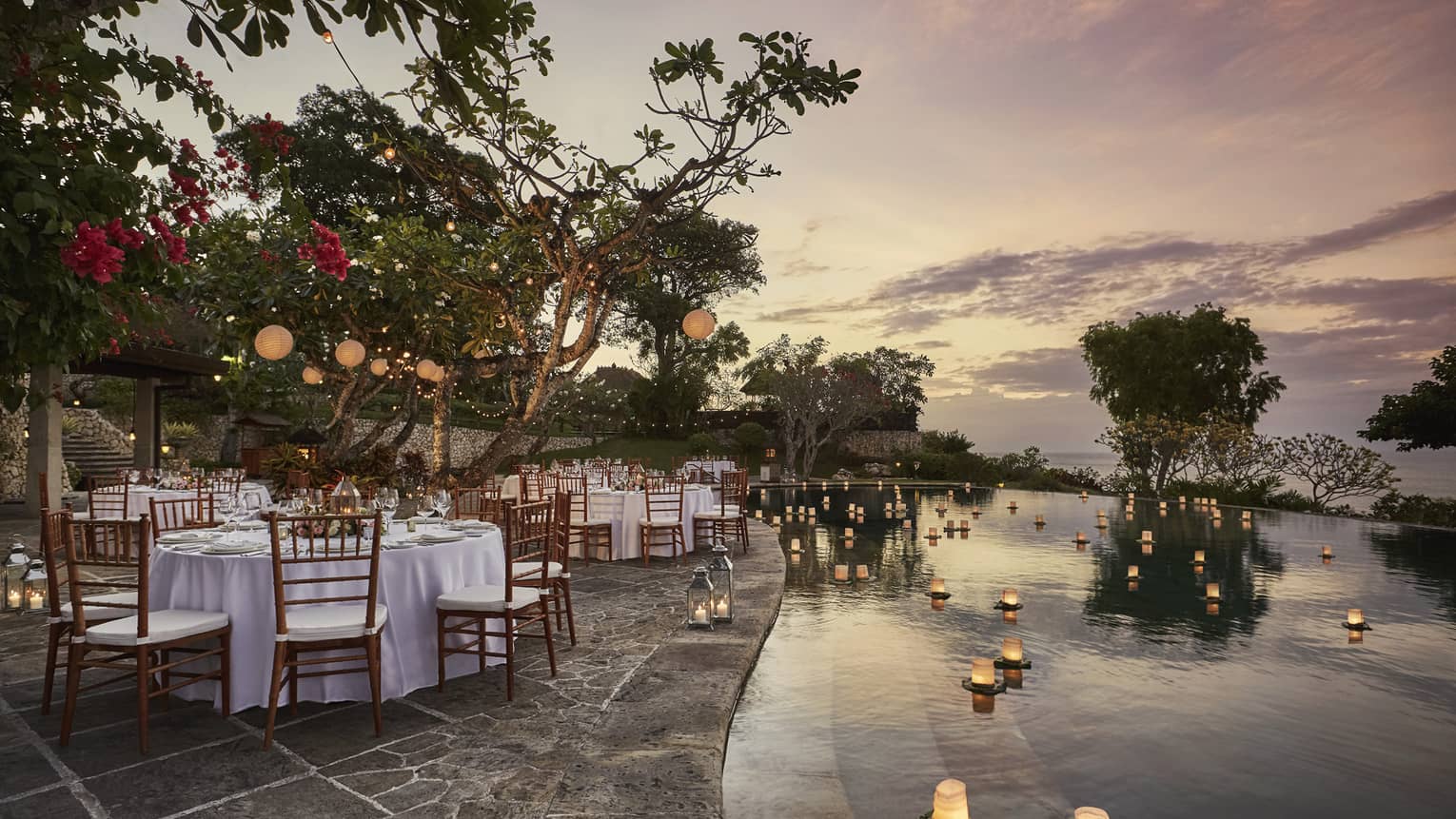 Pool Terrace banquet dining tables by candles floating on water at sunset