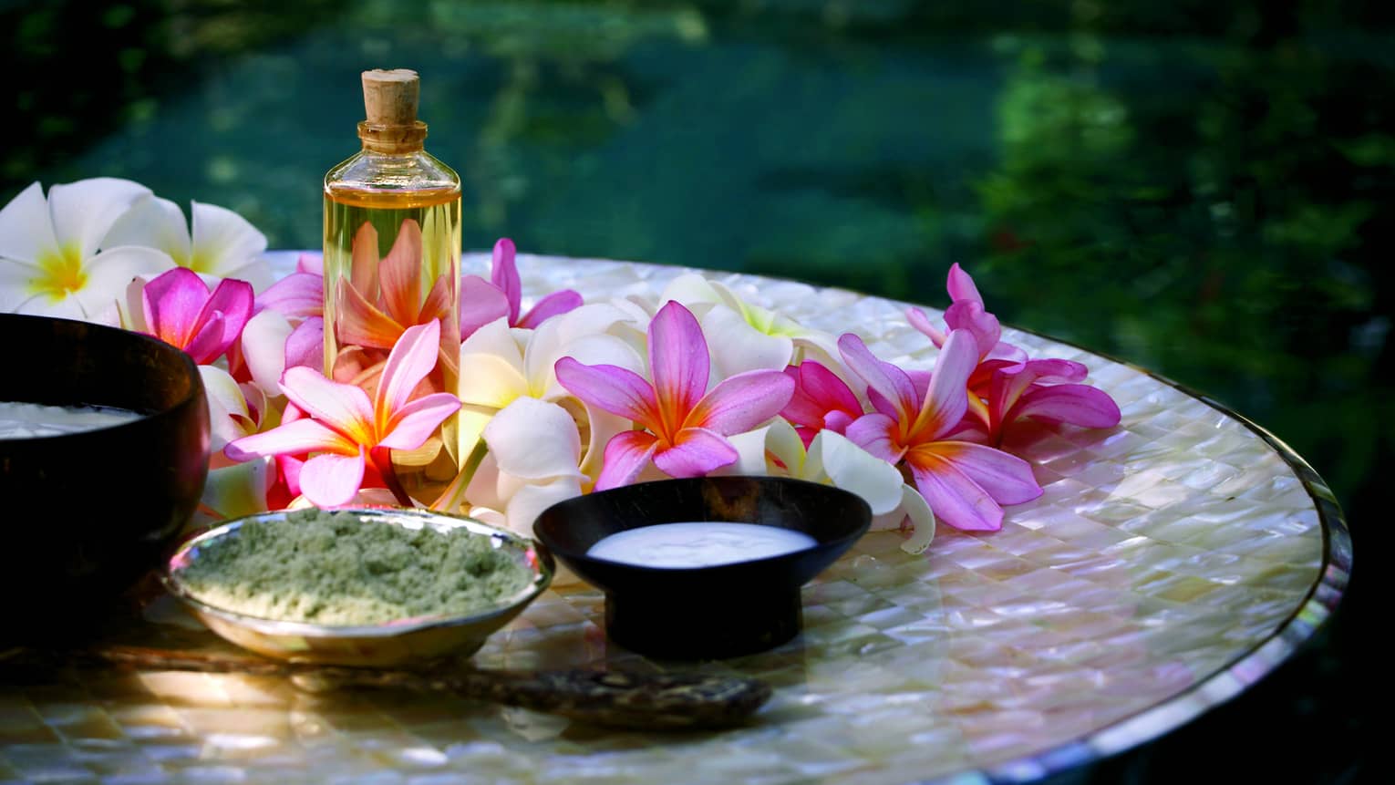 Spa tray with fresh pink and white flowers, glass bottle with oil and cork, small bowls of salt and lotion