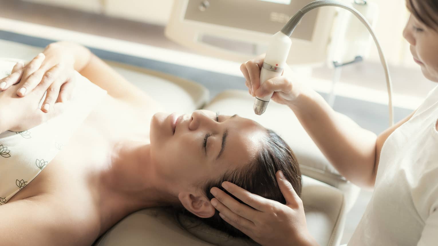 An aesthetician uses a tool on the face of a relaxing woman.
