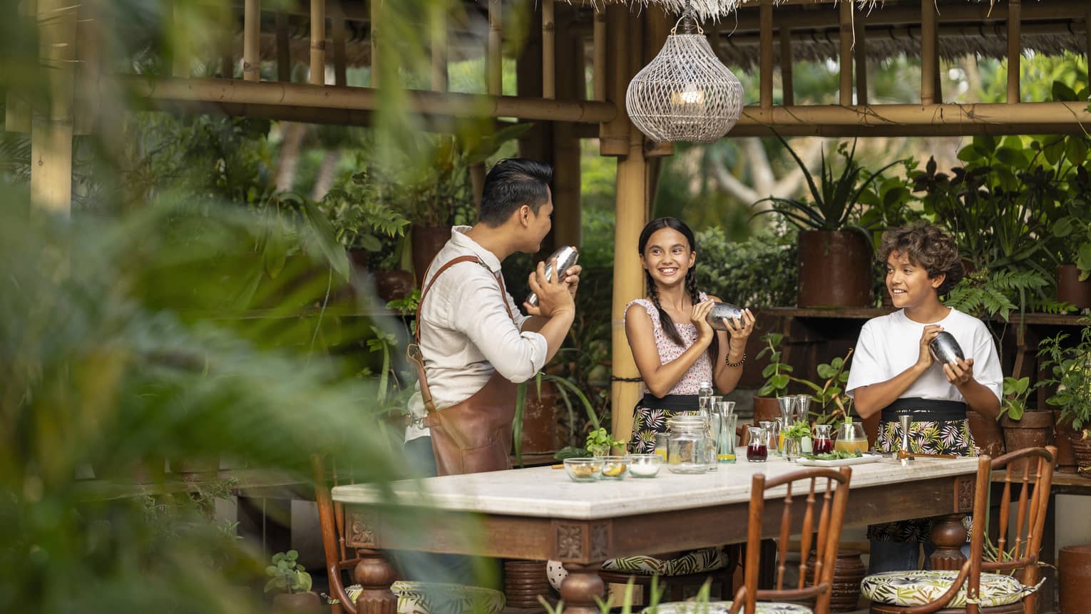 Two kids and adult instructor hold mocktail shakers during class at outdoor pavilion