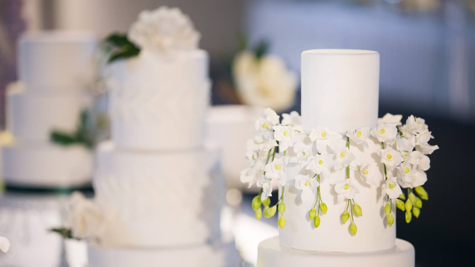 Three-tiered wedding cakes are each garnished with white florals 