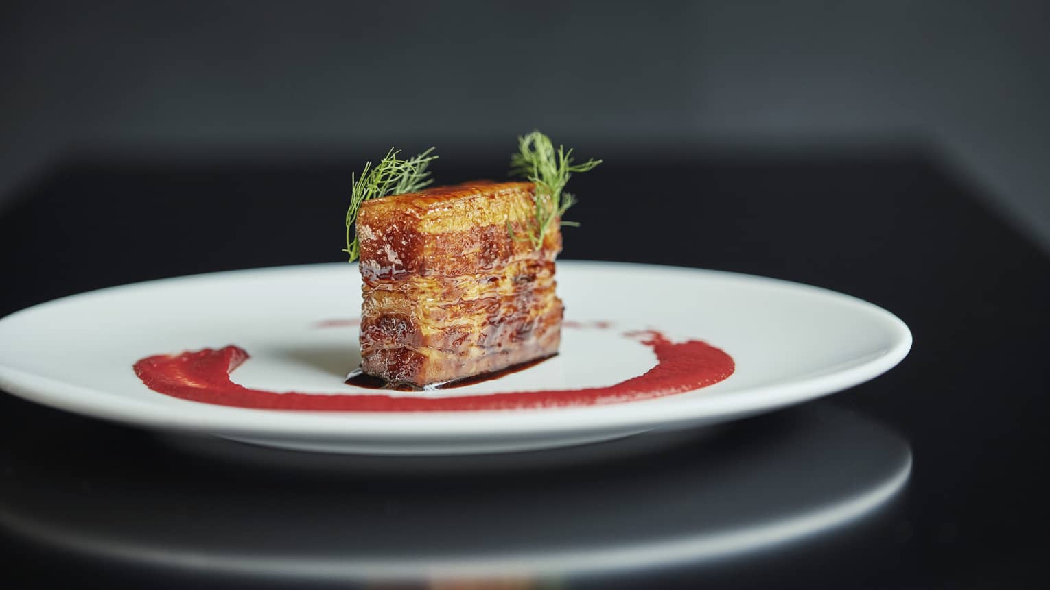 Pork belly slab on white plate with red sauce and green garnishes