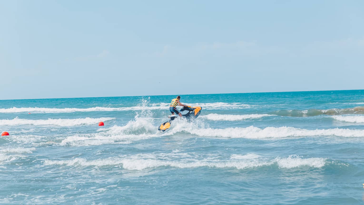 Person riding jet ski along waves in blue ocean