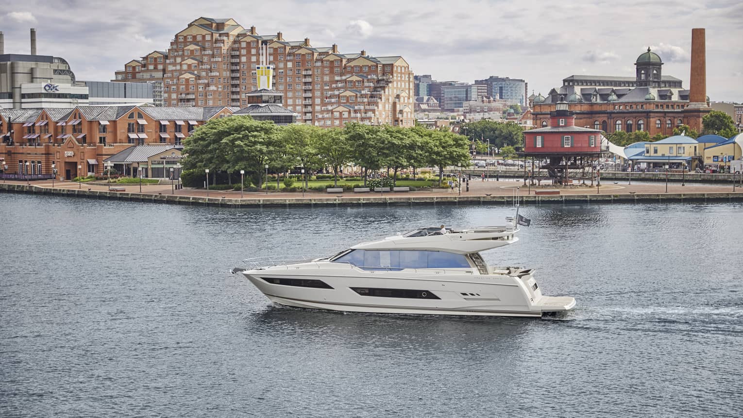 Small white yacht cruising along Baltimore Inner Harbor, past waterfront and buildings