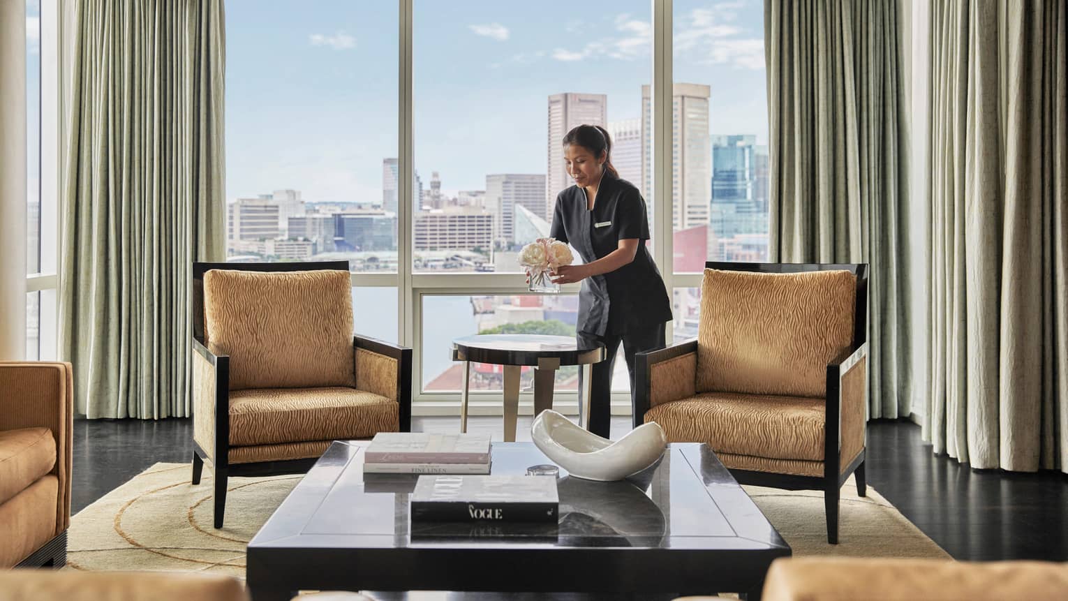 Woman cleaning a living room, with four gold-coloured, upholstered arm chairs, large coffee table