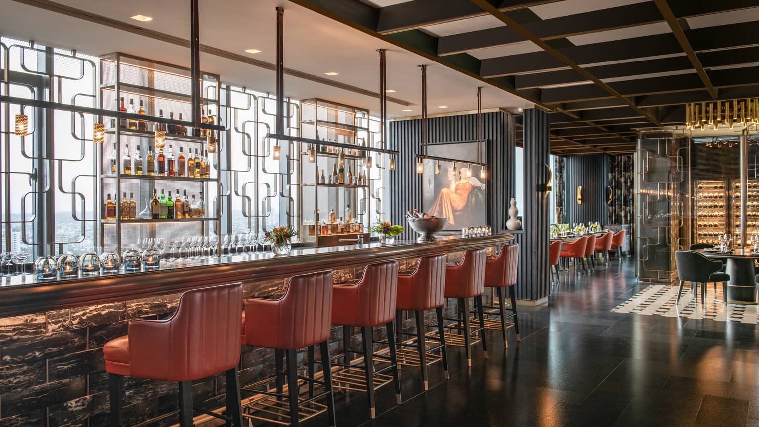 Interior of restaurant bar area with red leather high-backed chairs, glass display of liquor bottles behind bar, and dark wood floors and panelling