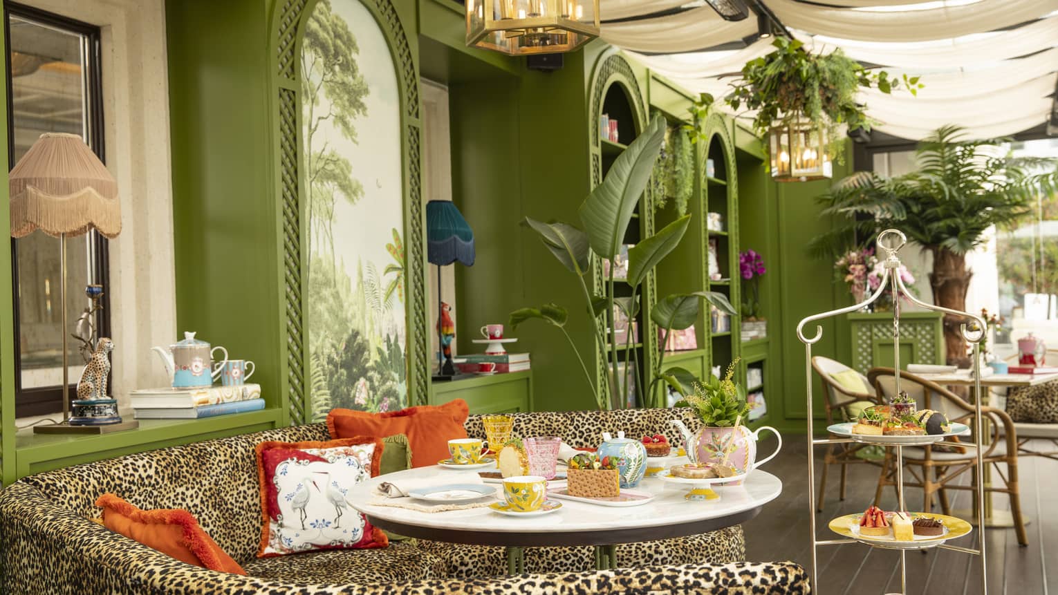 Gracebrands Patisserie setup by curved leopard-print couch topped with orange pillows and green walls in backdrop