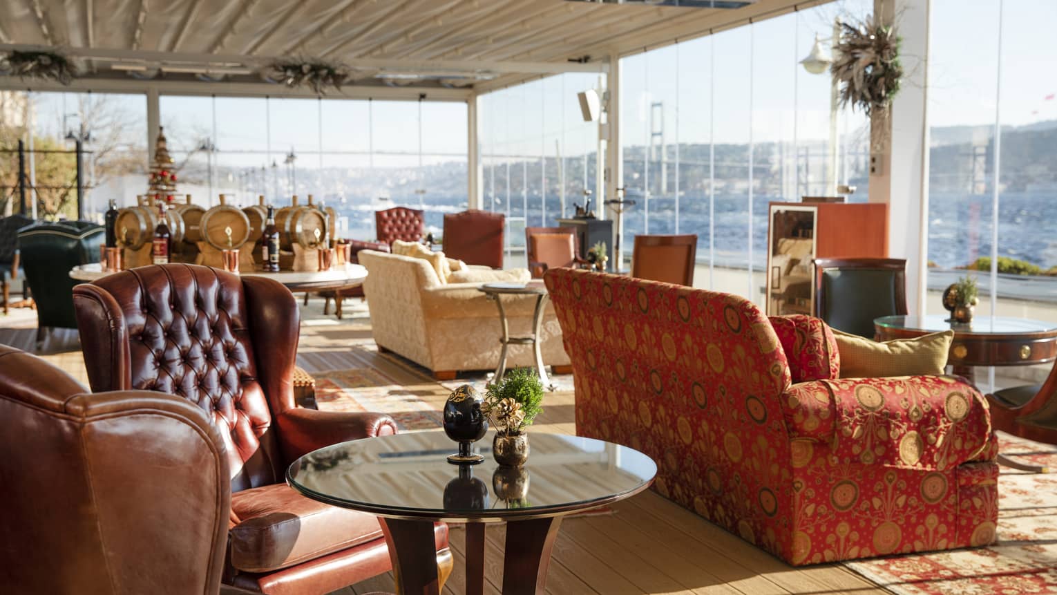 Lounge area with large leather wing chairs and couches facing tall windows looking out to water views