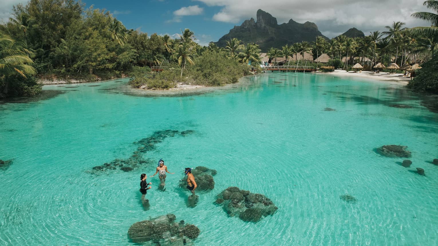 Aerial view of three guests standing in the clear turquoise water of the lagoon at the Dive Centre