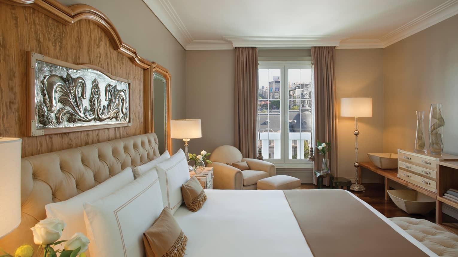 Owner Suite bed with tall wood headboard and silver plaque, white armchair by window