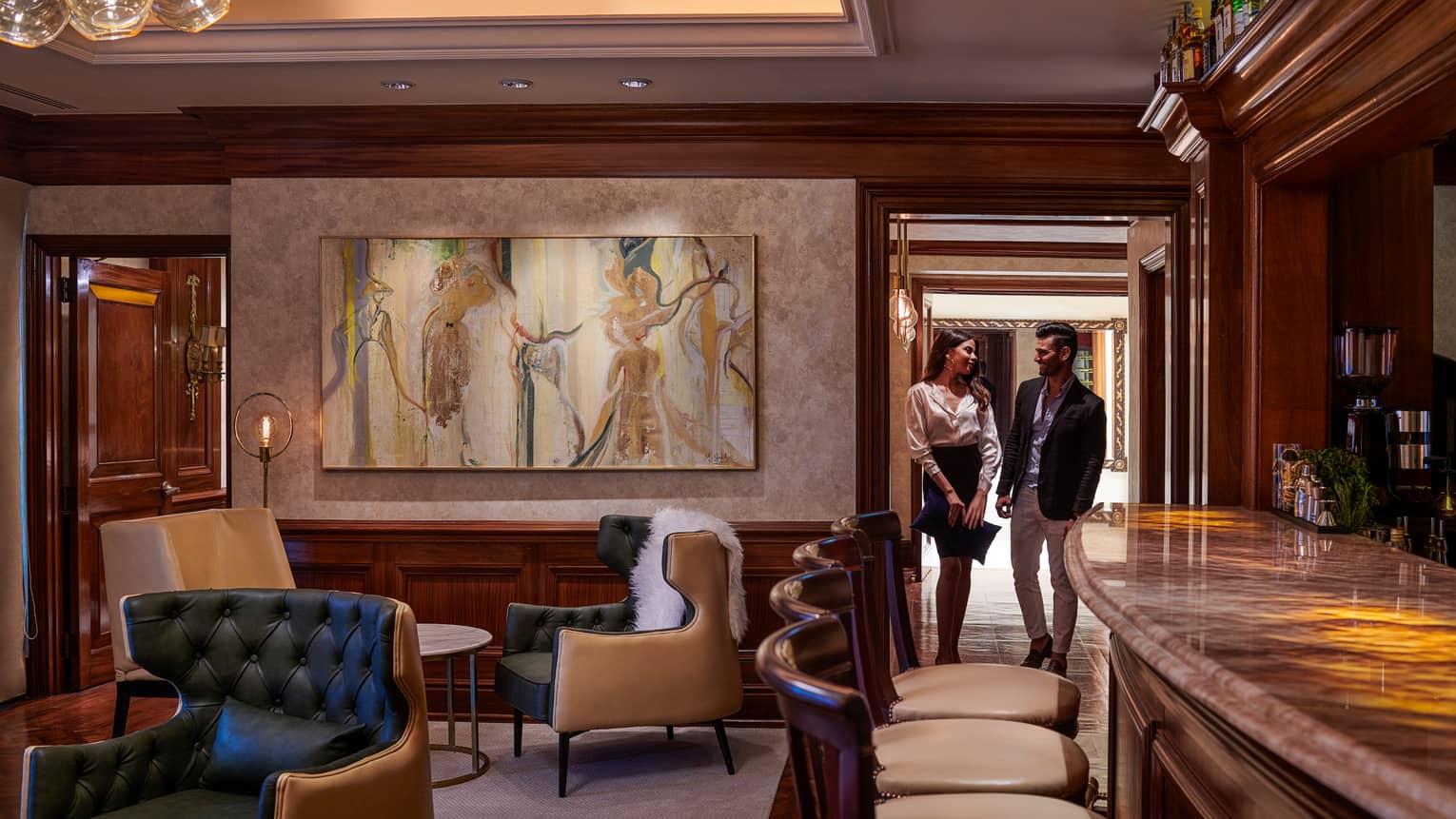 Woman and man walk through door into cocktail lounge with large painting, leather chairs