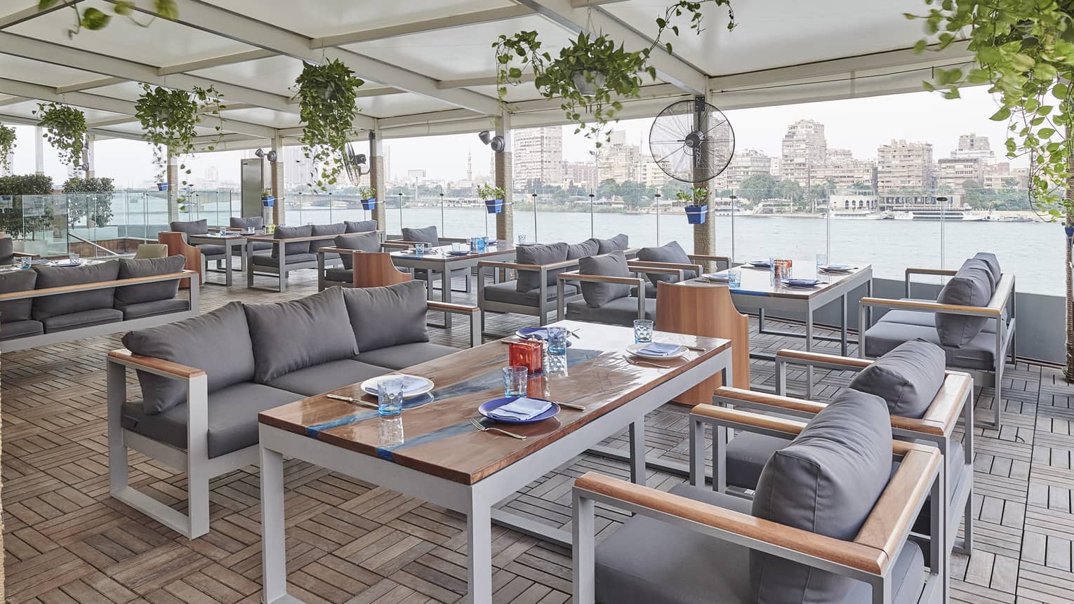 Zoe restaurant dining room with rectangular tables and grey couch-style seating, wall of windows with Nile views
