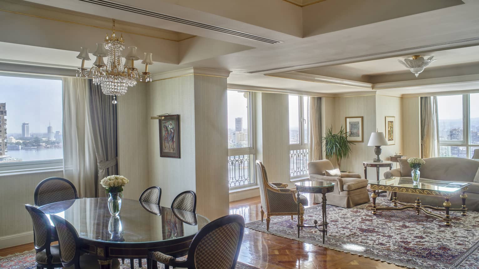 Guest room living and dining area with tan sofa and armchair, oval table with six chairs, floor-to-ceiling windows with city views