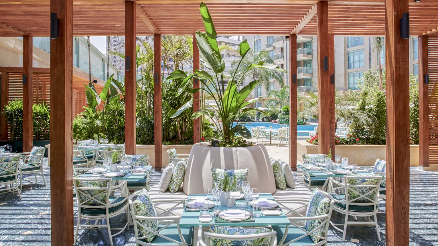 Byblos restaurant outdoor dining space with wooden columns, rattan chairs and square tables, large potted plant in middle