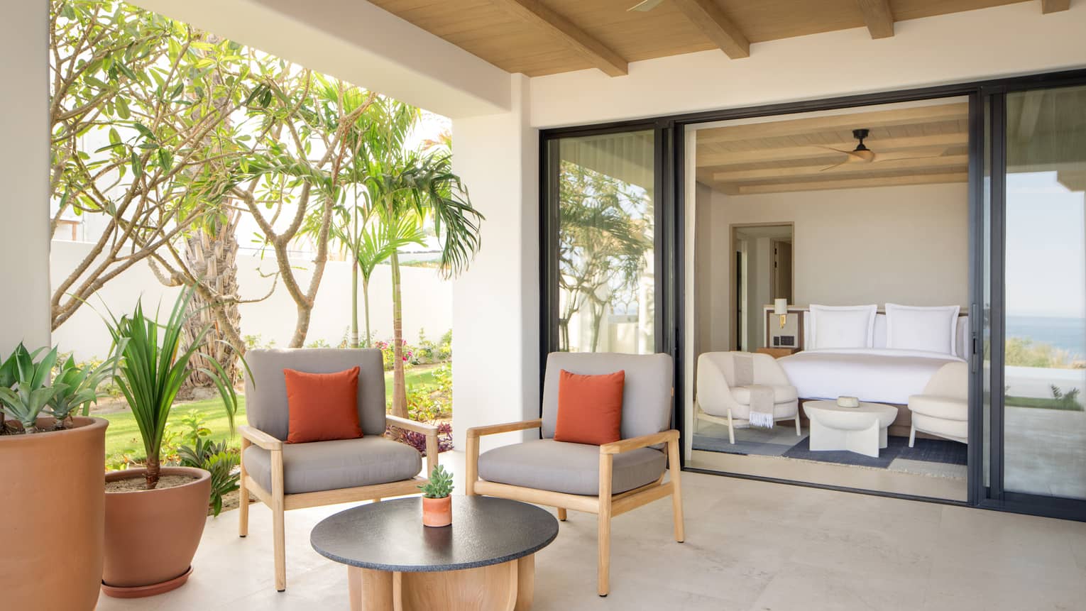 Covered terrace with two chairs and a small table, leading into a bedroom with king bed and chairs at luxury resort