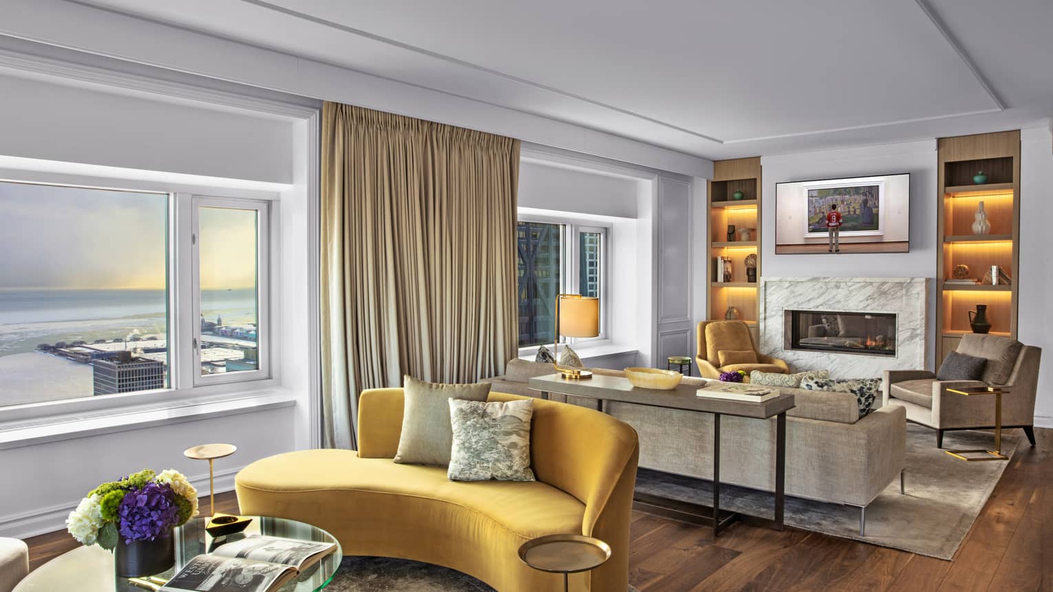 Suite with a yellow couch and glass table, as well as a television and fireplace.