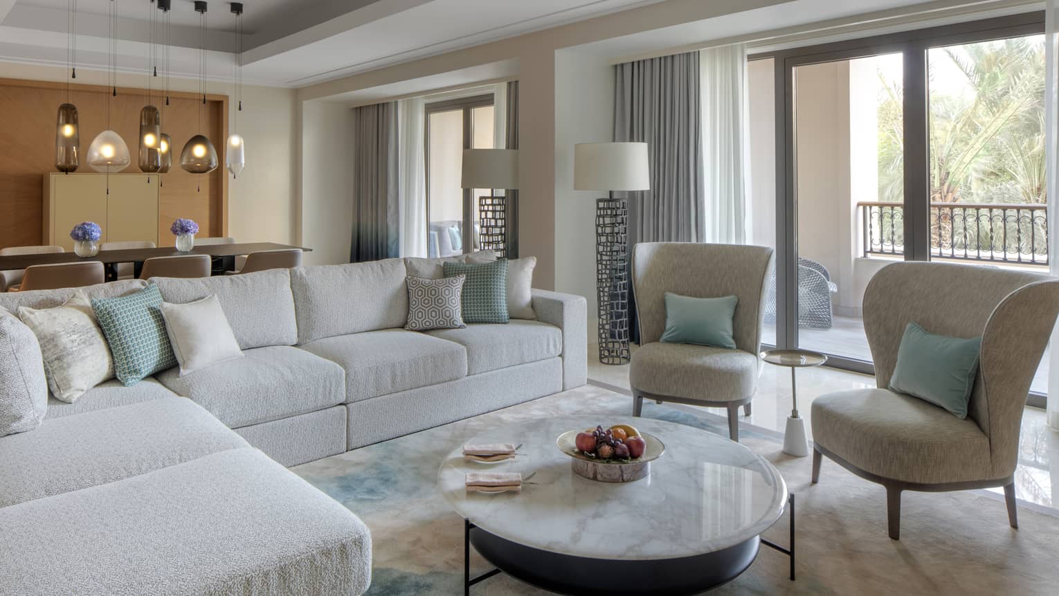 Living room with light beige sectional sofa, two cushioned chairs, round coffee table, balcony