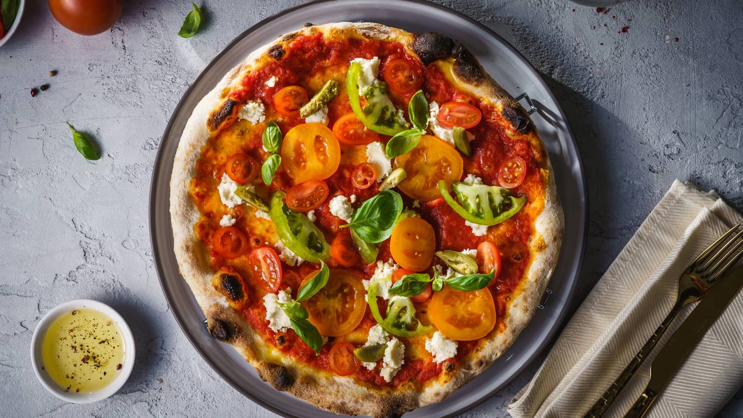 A pizza covered in tomatoes, peppers and spinach served on a grey plate.
