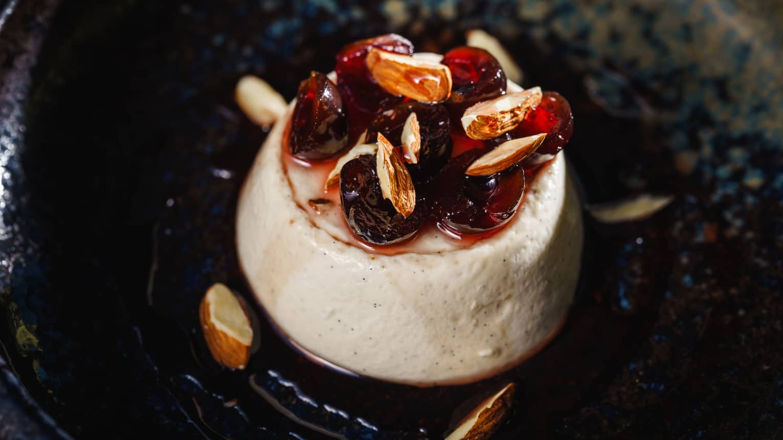 A dollop of cream with sliced dates and nuts served on a black dish.