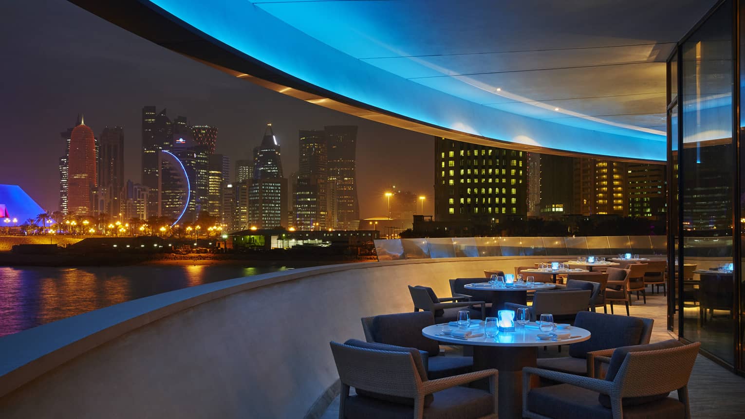 Curved Nobu restaurant patio with dining tables at night, skyline views, blue lights 
