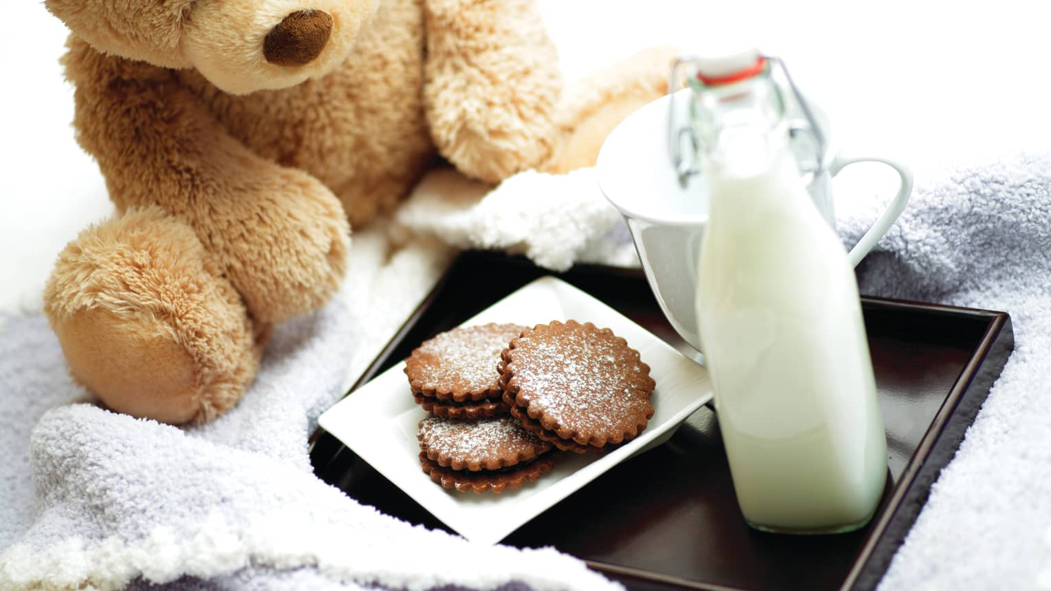 A teddy bear next to a tray of milk and cookies.