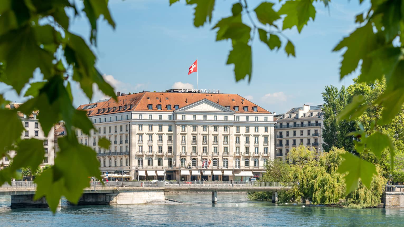 Four Seasons Hotel Geneva surrounded by green foliage, Lake Geneva in the foreground