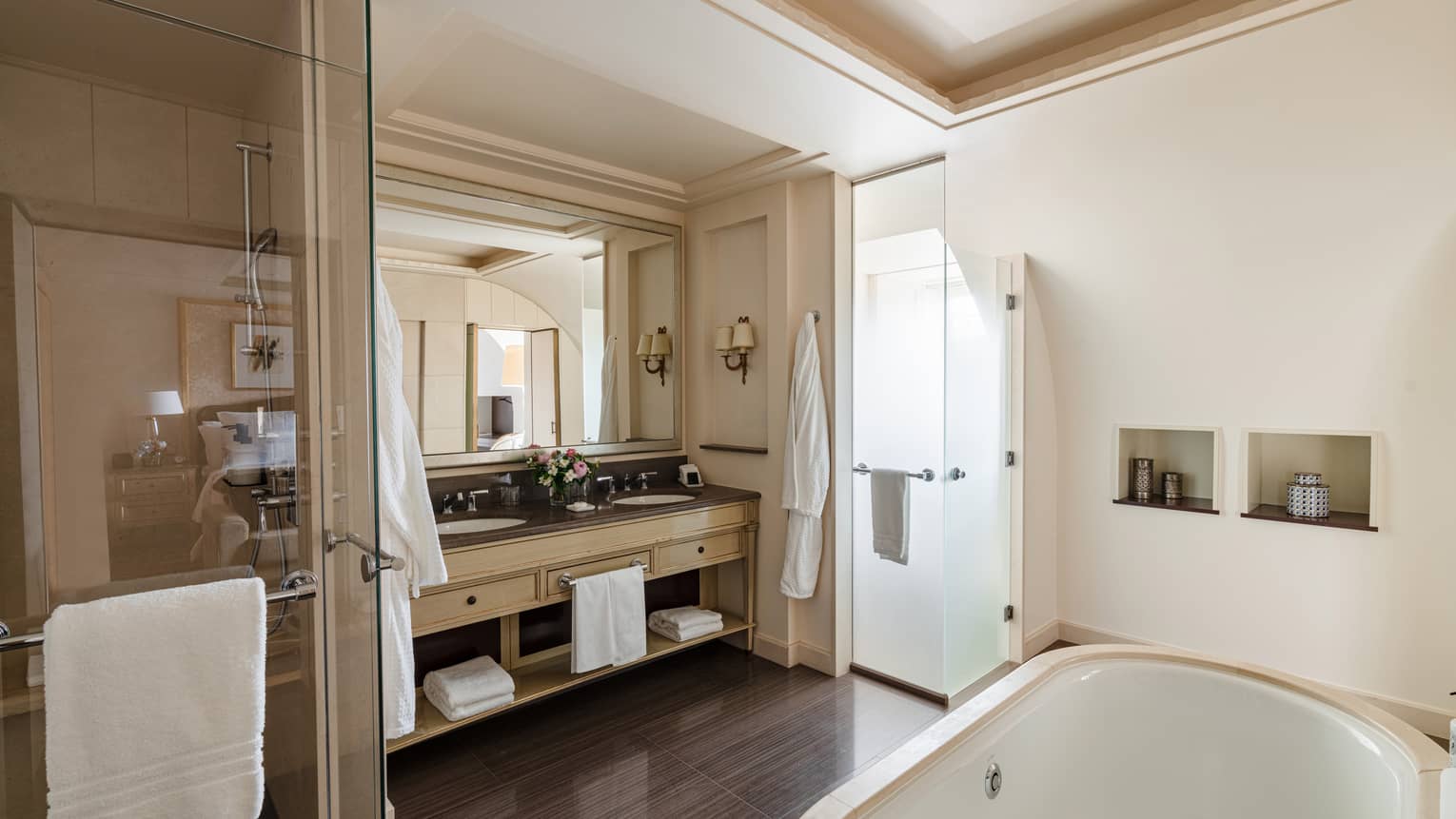 Luxury hotel bathroom with a large mirror, double sink vanity, glass shower and a bathtub in a neutral-toned setting