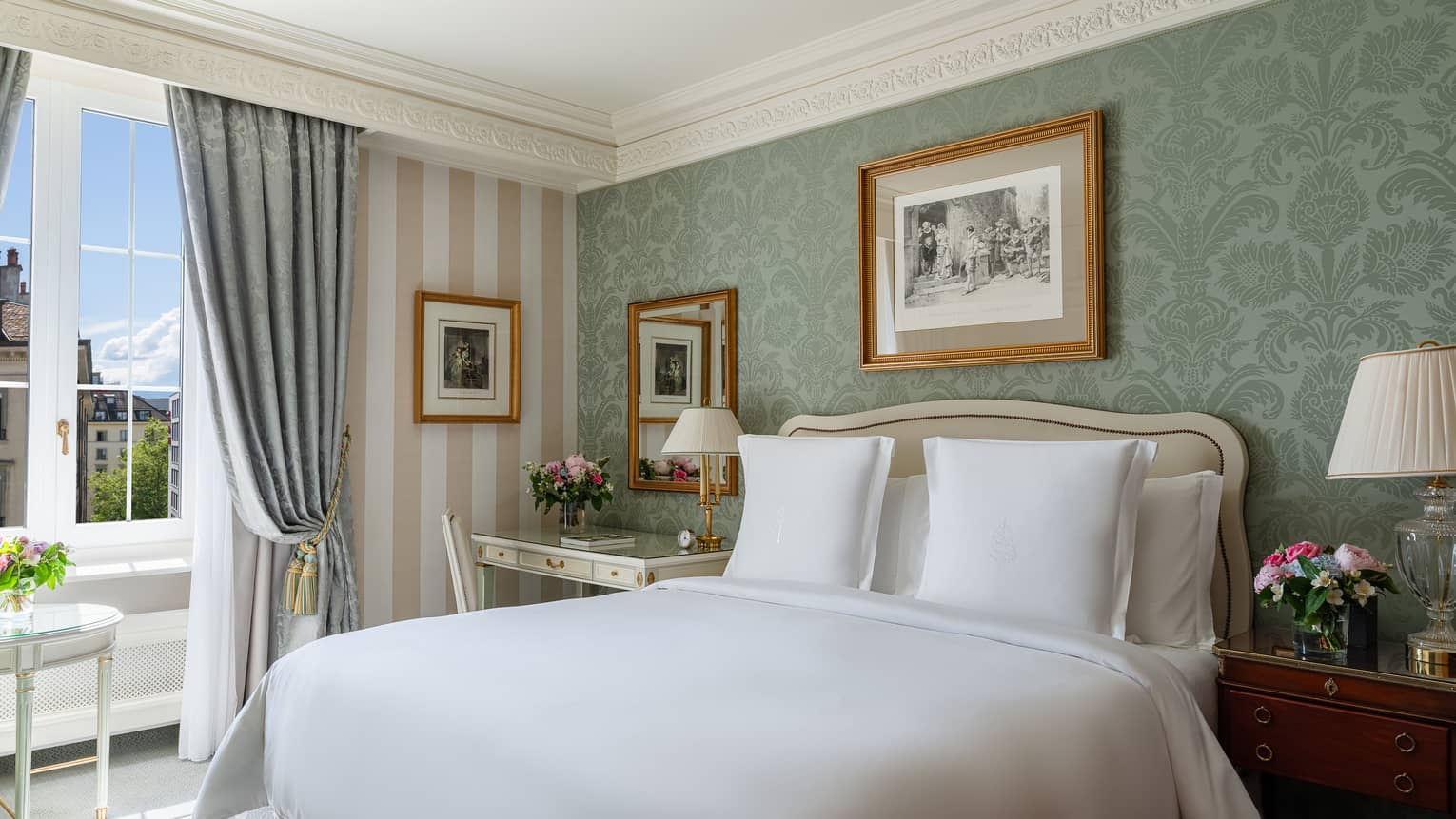 Luxury hotel room with a king bed, desk, bedside table, framed artwork and a window with city view